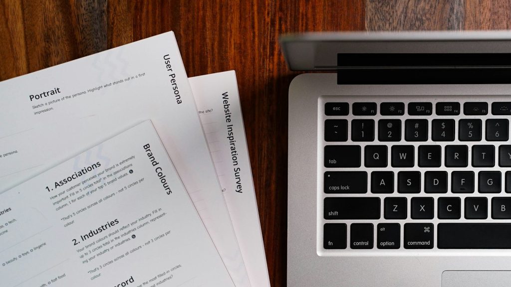 Laptop beside printed documents on a wooden table