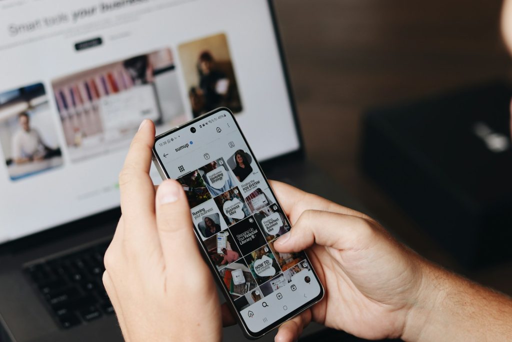 Person using social media on a smartphone in front of a laptop