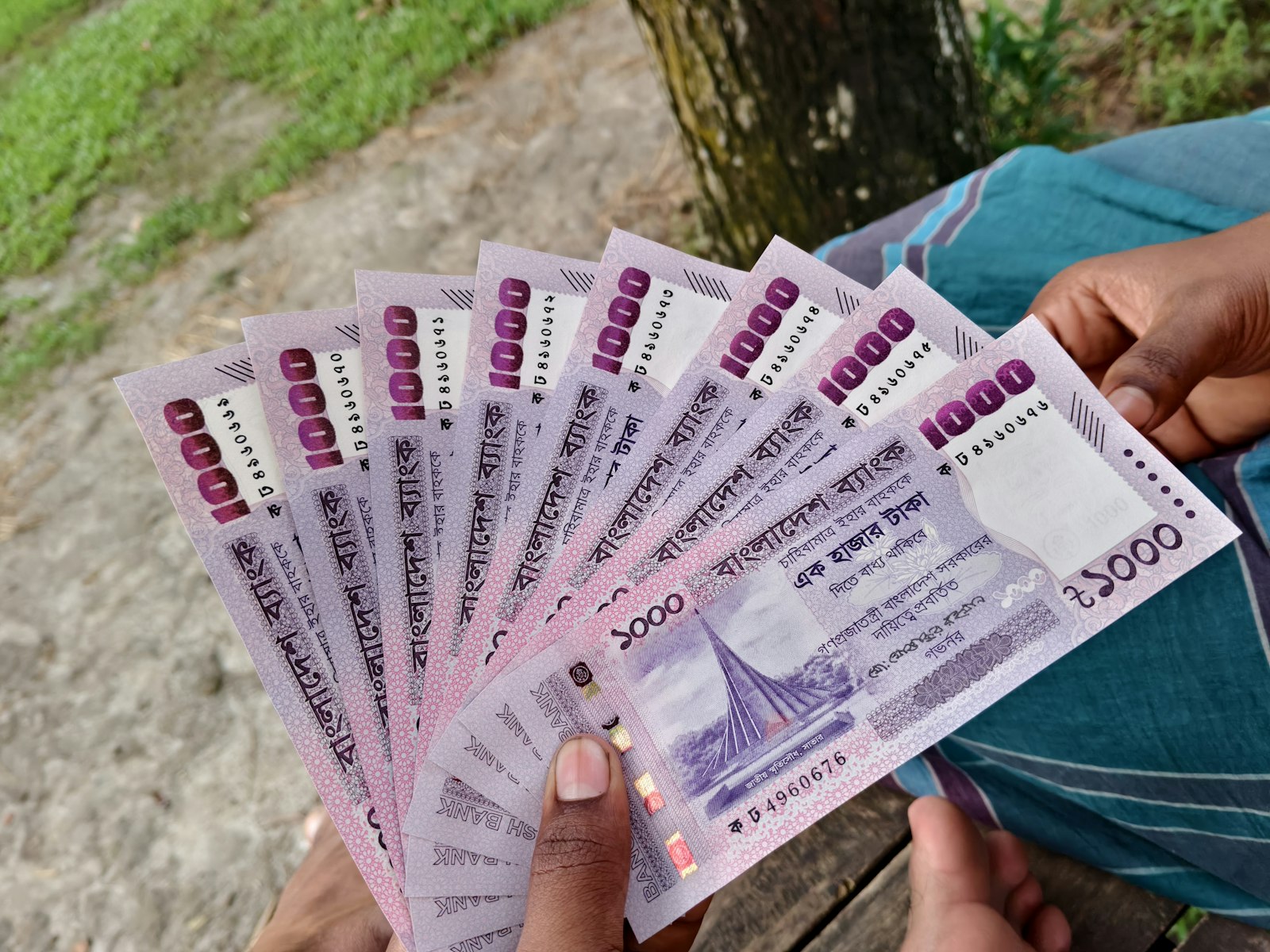 Hands holding a fan of 1000 Bangladeshi taka banknotes