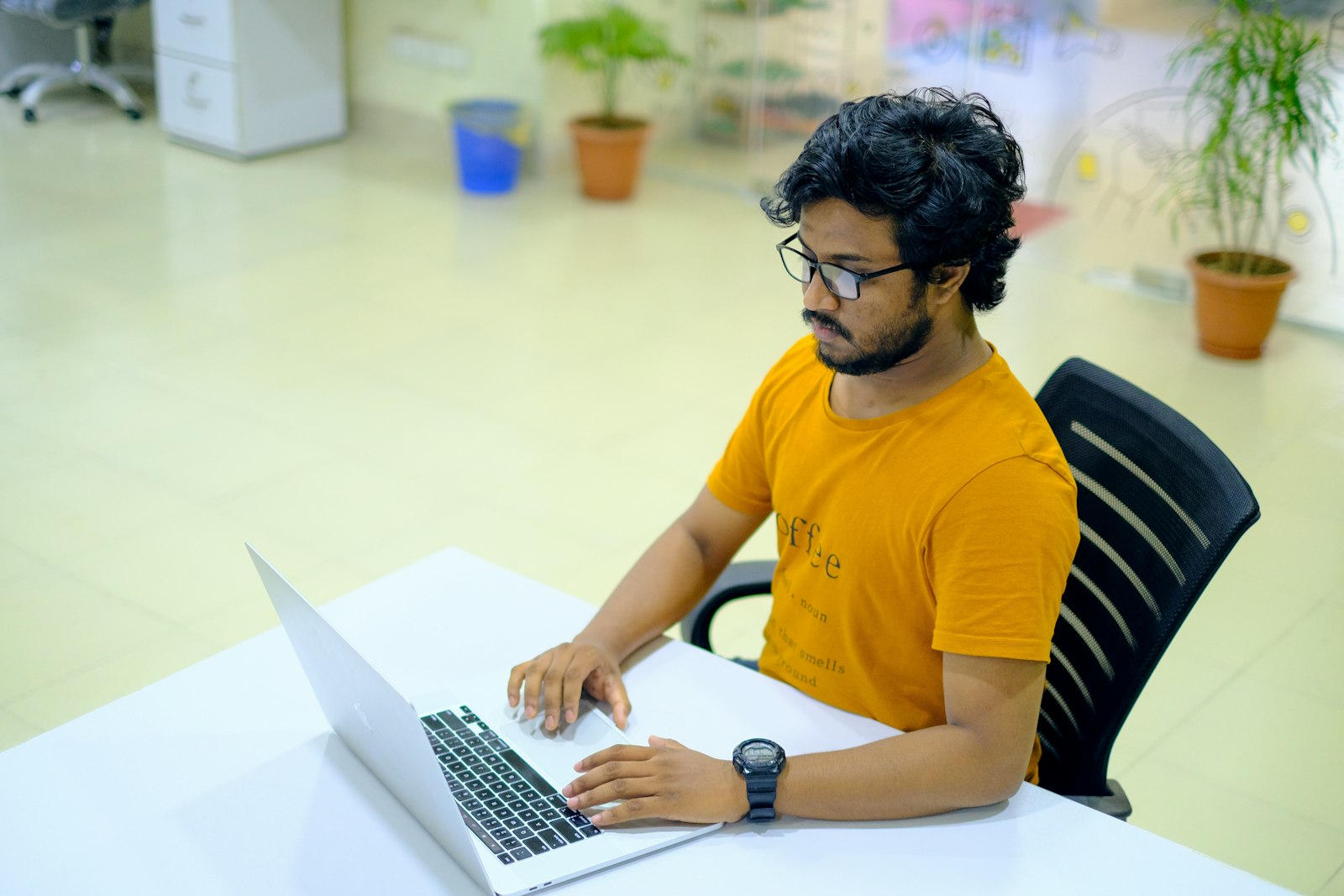 Young freelancer in a yellow T-shirt working on a laptop at a bright office desk