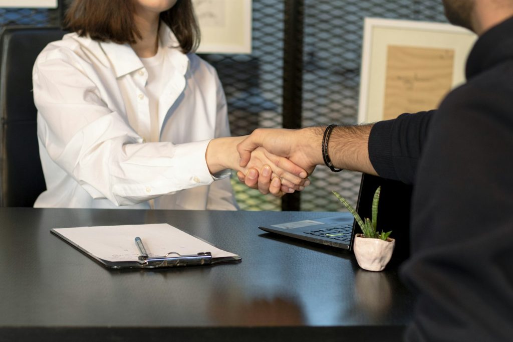 Two people shaking hands over a laptop after agreeing a project