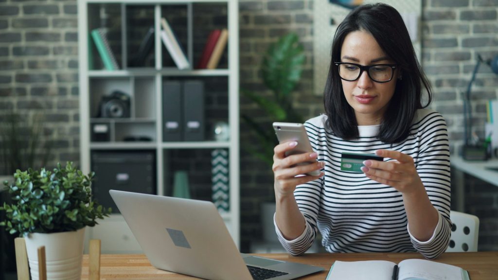 Woman checking a payment on her phone beside a laptop