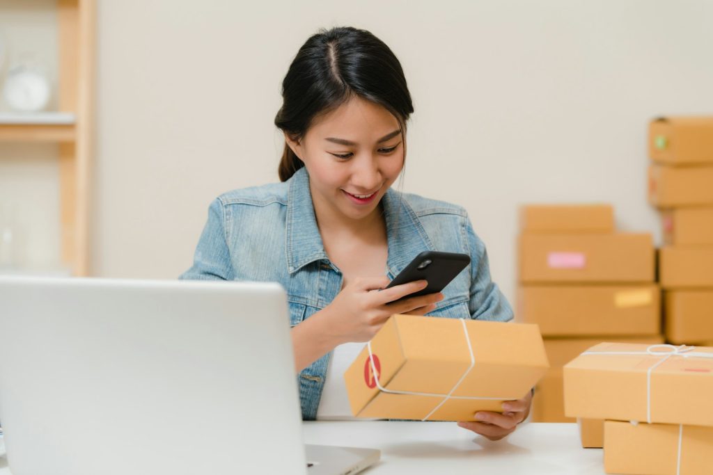 Woman checking an order on her phone beside packed boxes